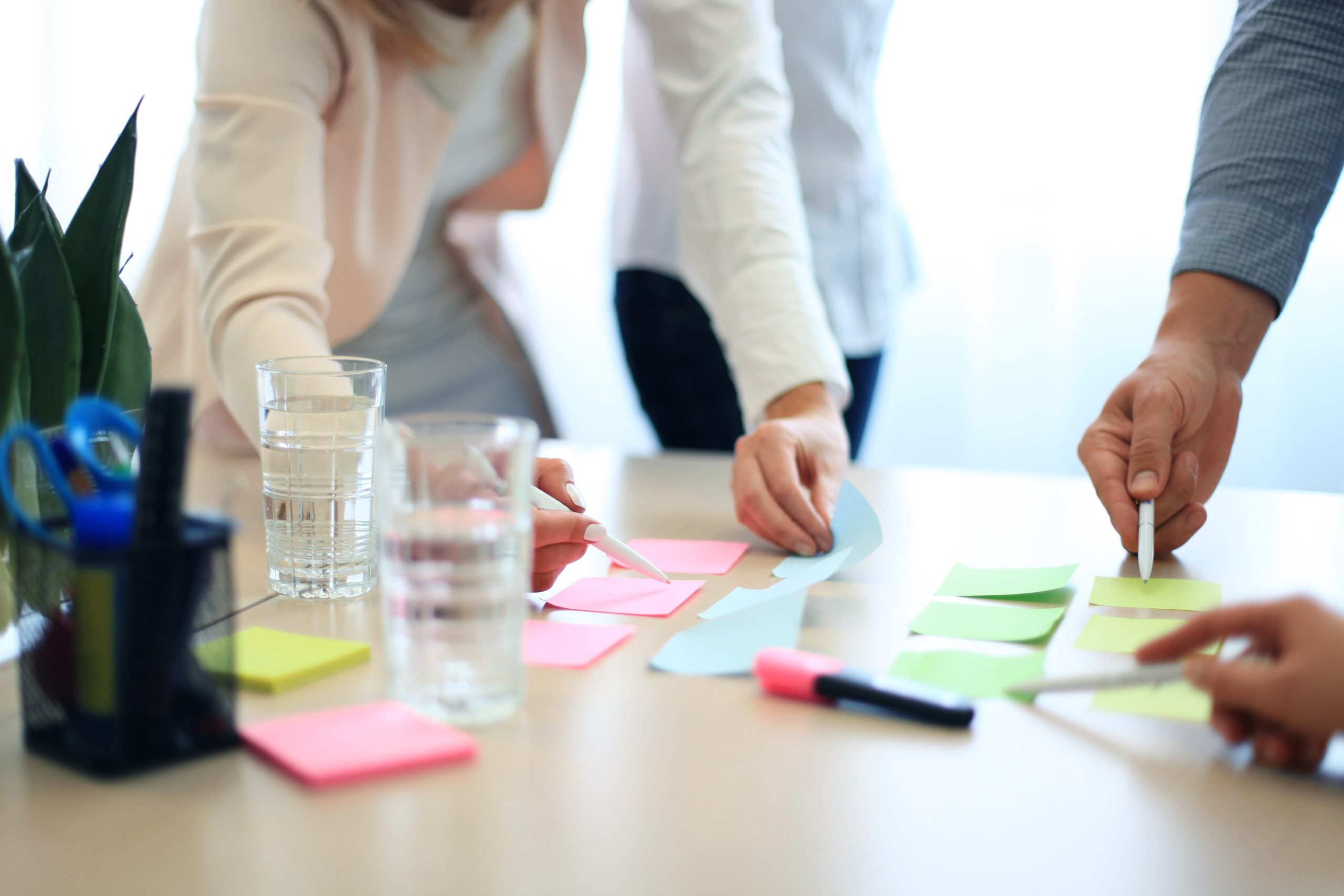 three hands writing on sticky notes